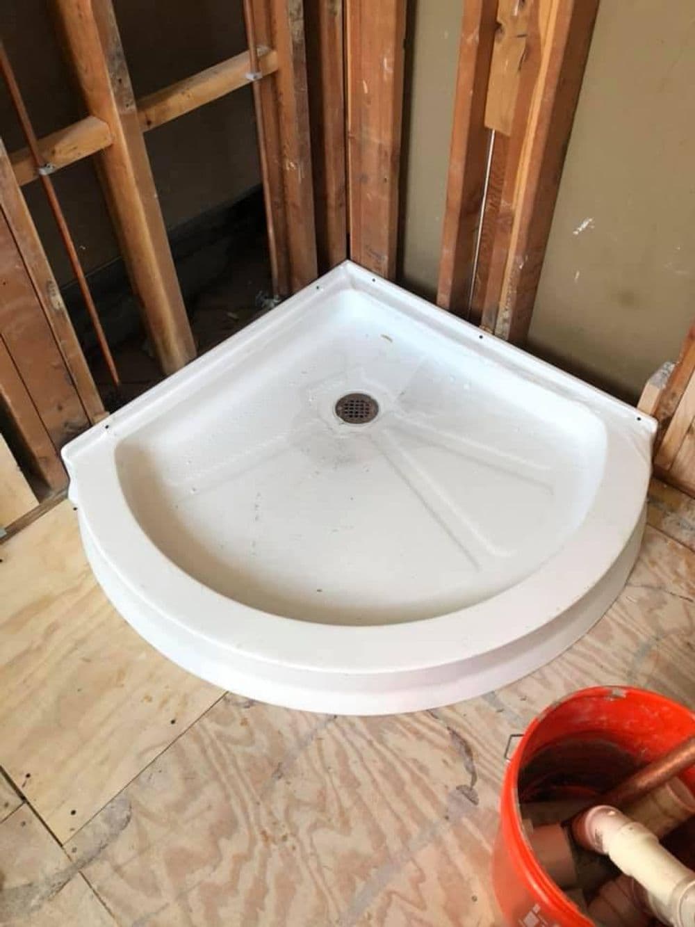 Corner shower pan installed in a partially renovated bathroom with exposed framing.
