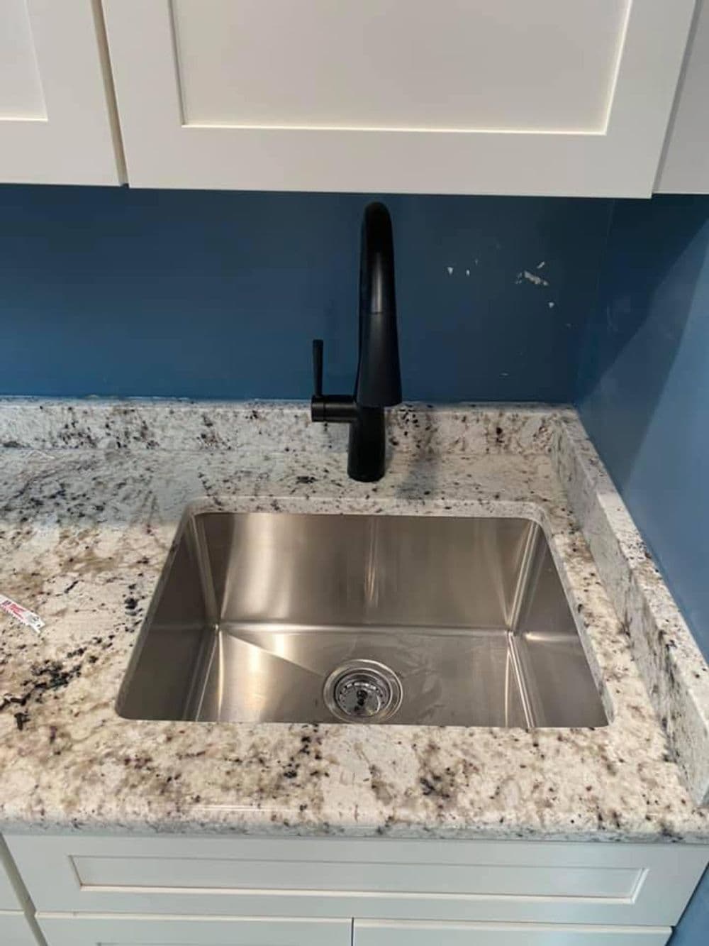 Stainless steel kitchen sink with modern black faucet and granite countertop.
