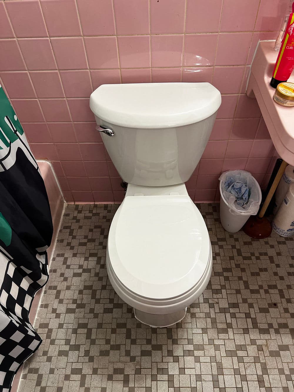 Modern white toilet in a pink tiled bathroom with checkered shower curtain.