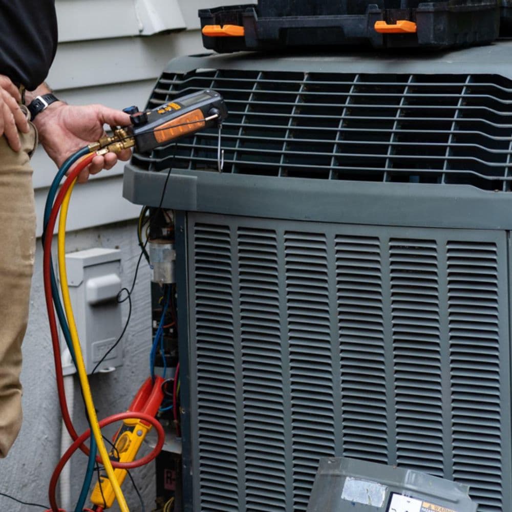 Technician measuring pressure on residential HVAC unit with gauges and tools.