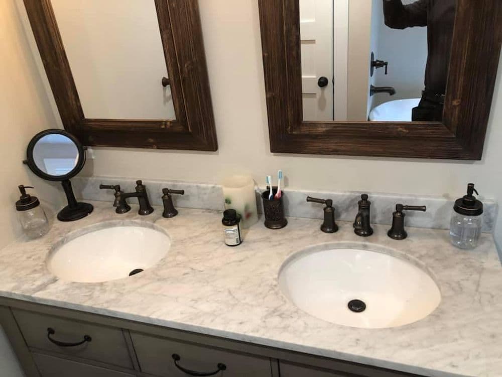 Double bathroom vanity with marble countertop, bronze faucets, and mirrors. Organized accessories.