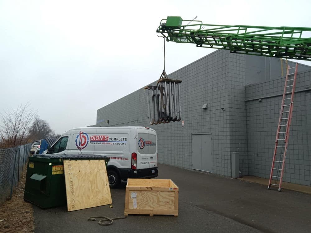 Dion's Complete Plumbing van unloading equipment near dumpster and wooden crate in industrial area.
