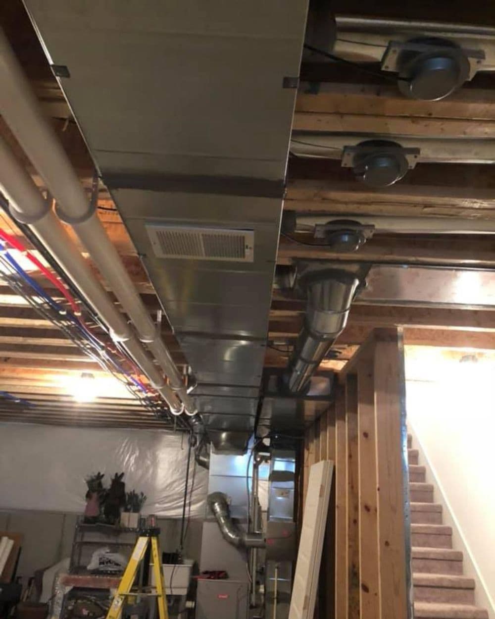 Ductwork installation in a basement with exposed beams and construction materials.