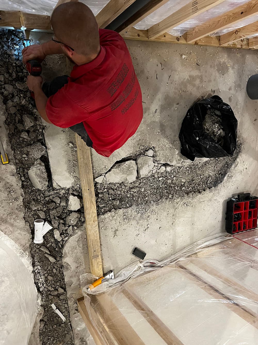 Construction worker repairing cracked concrete floor in a basement with tools and debris.