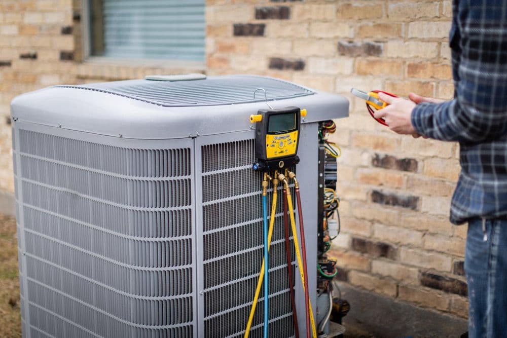 Technician measuring HVAC unit with manifold gauge for maintenance and repair.