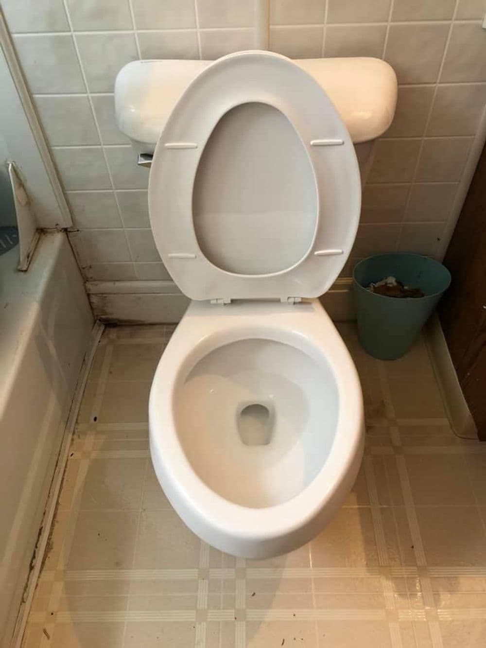 Clean white toilet in a bathroom setting with tiled floor and nearby trash can.