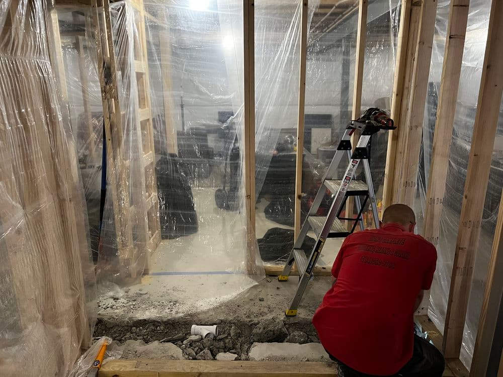 Construction worker in a basement renovation, installing framing and plastic barriers for moisture control.