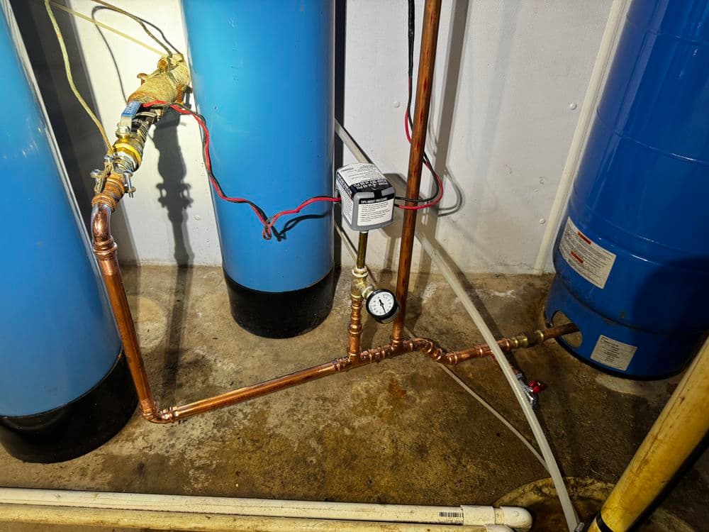 Copper piping installation with pressure gauge connected to blue water tanks in basement.