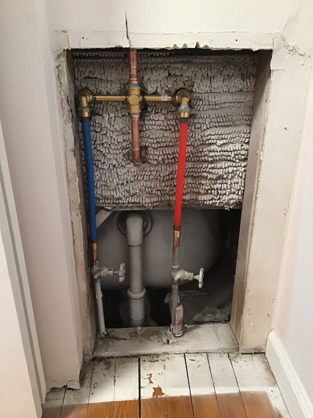 Visible plumbing access panel with blue and red pipes connected to valves in a wall.