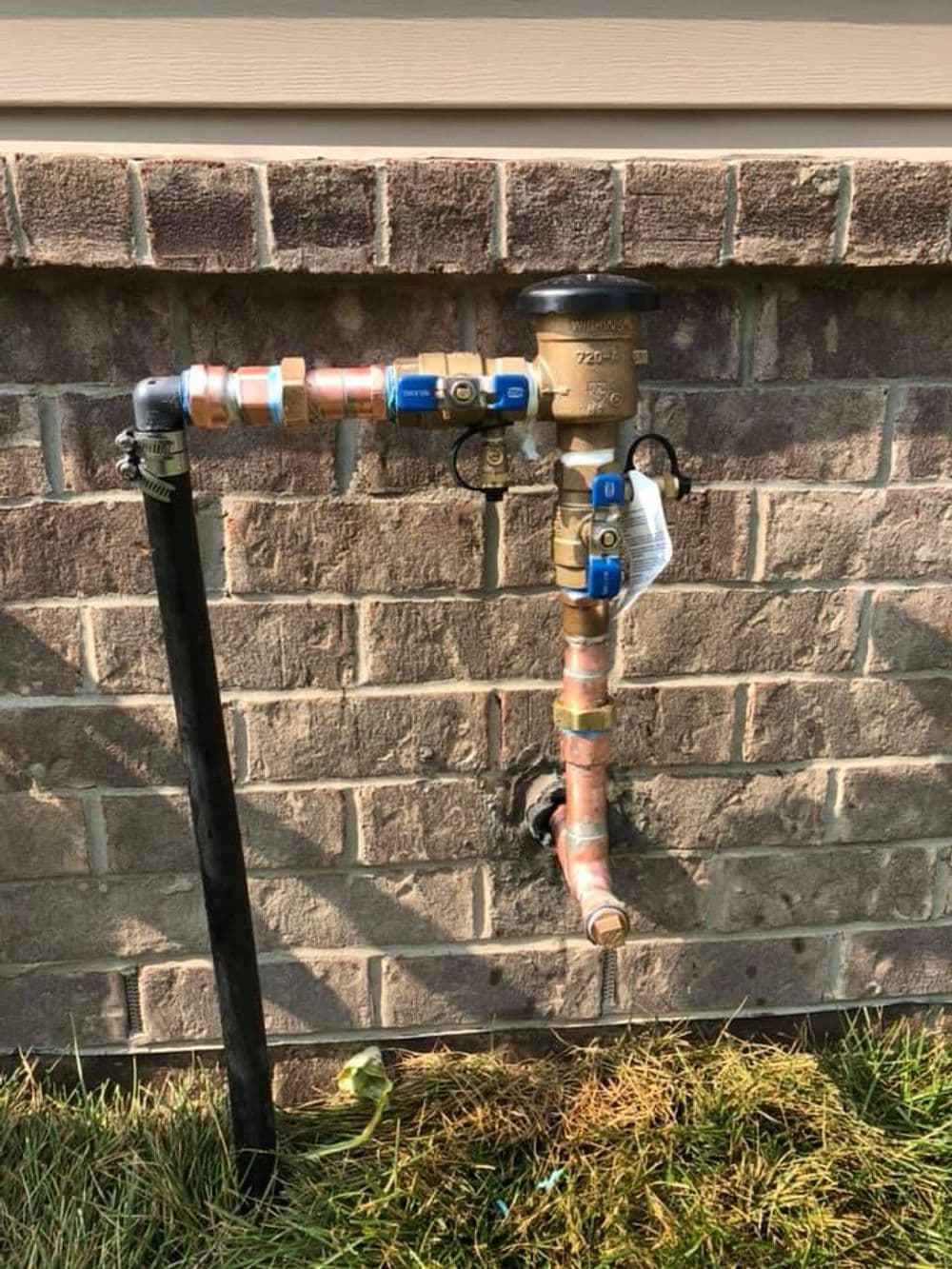 Water meter and copper piping installation against a brick wall, in a residential setting.