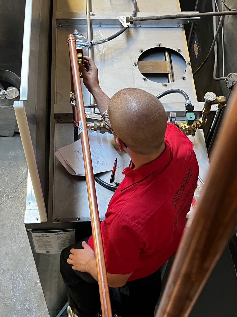 Plumber installing copper pipes and checking blueprints in a commercial setting.