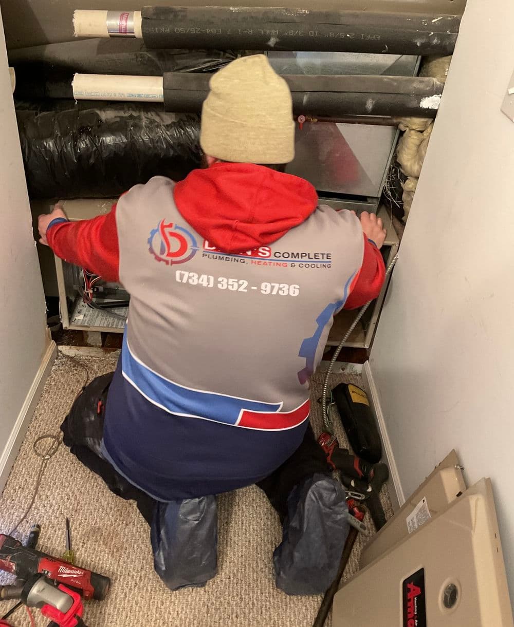 Plumber wearing branded jacket working on heating system in residential space.