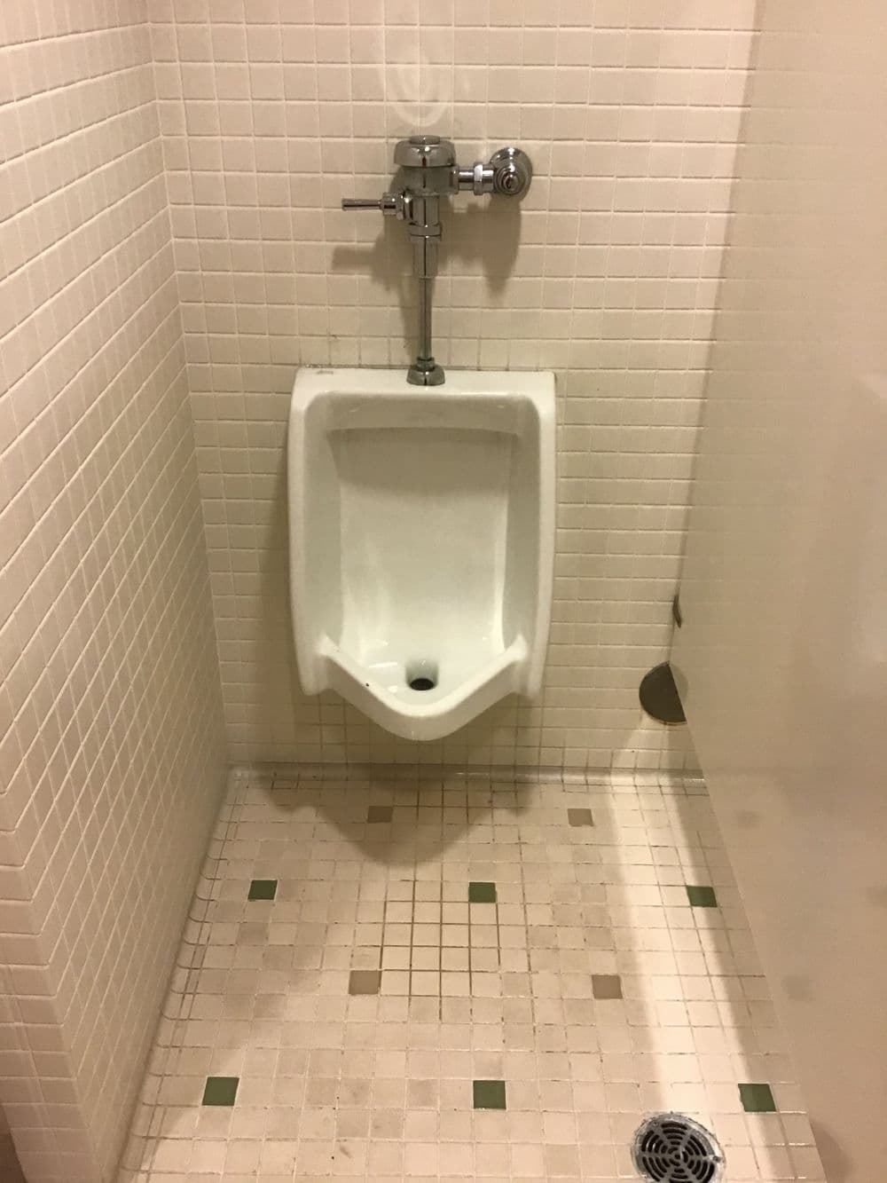 Men's restroom urinal in tiled setting with modern design and clean aesthetic.