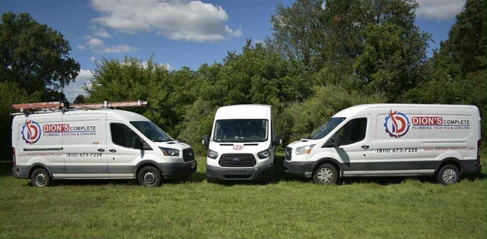 Three plumbing service vans from Dion's Complete, parked in a green field under a blue sky.