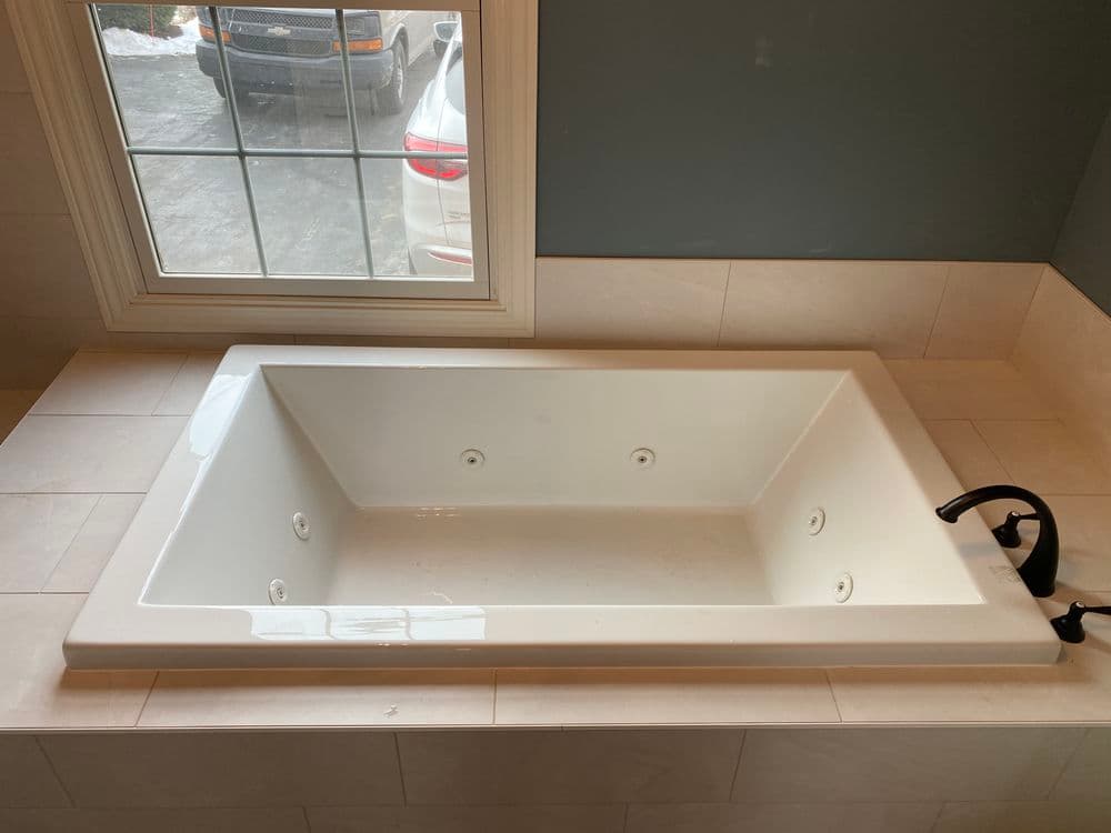 Modern white soaking tub with jets in a bright bathroom setting, natural light from window.