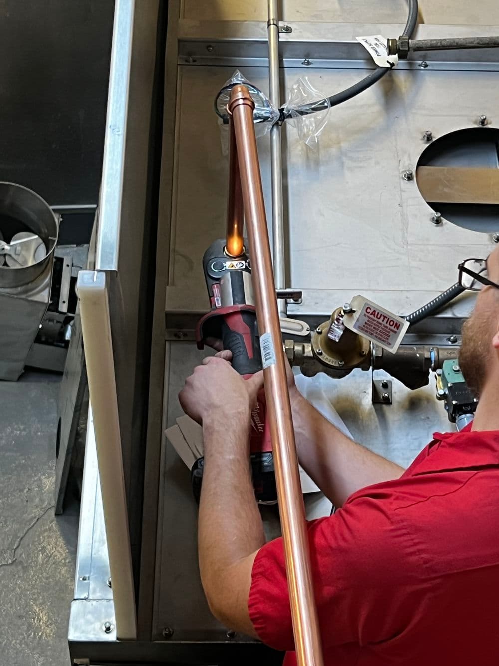 Technician soldering copper pipe with torch in workshop setting, focused on precision work.