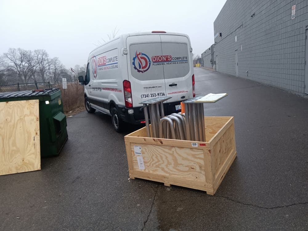 Dion's Complete Plumbing van with metal pipes in a wooden crate near a dumpster.