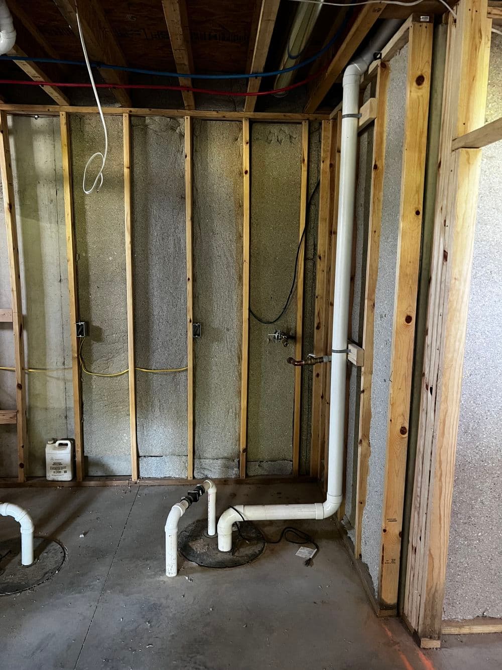 Unfinished basement plumbing setup with white PVC pipes and exposed wooden framing.