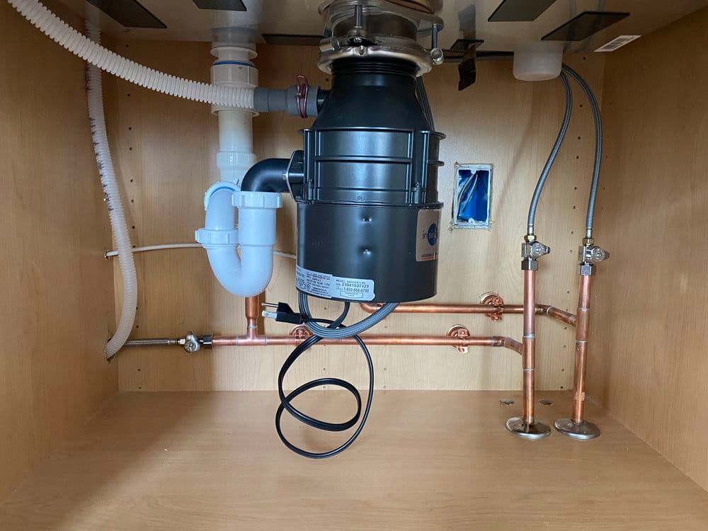 Under-sink garbage disposal installation with plumbing connections and copper pipes visible.