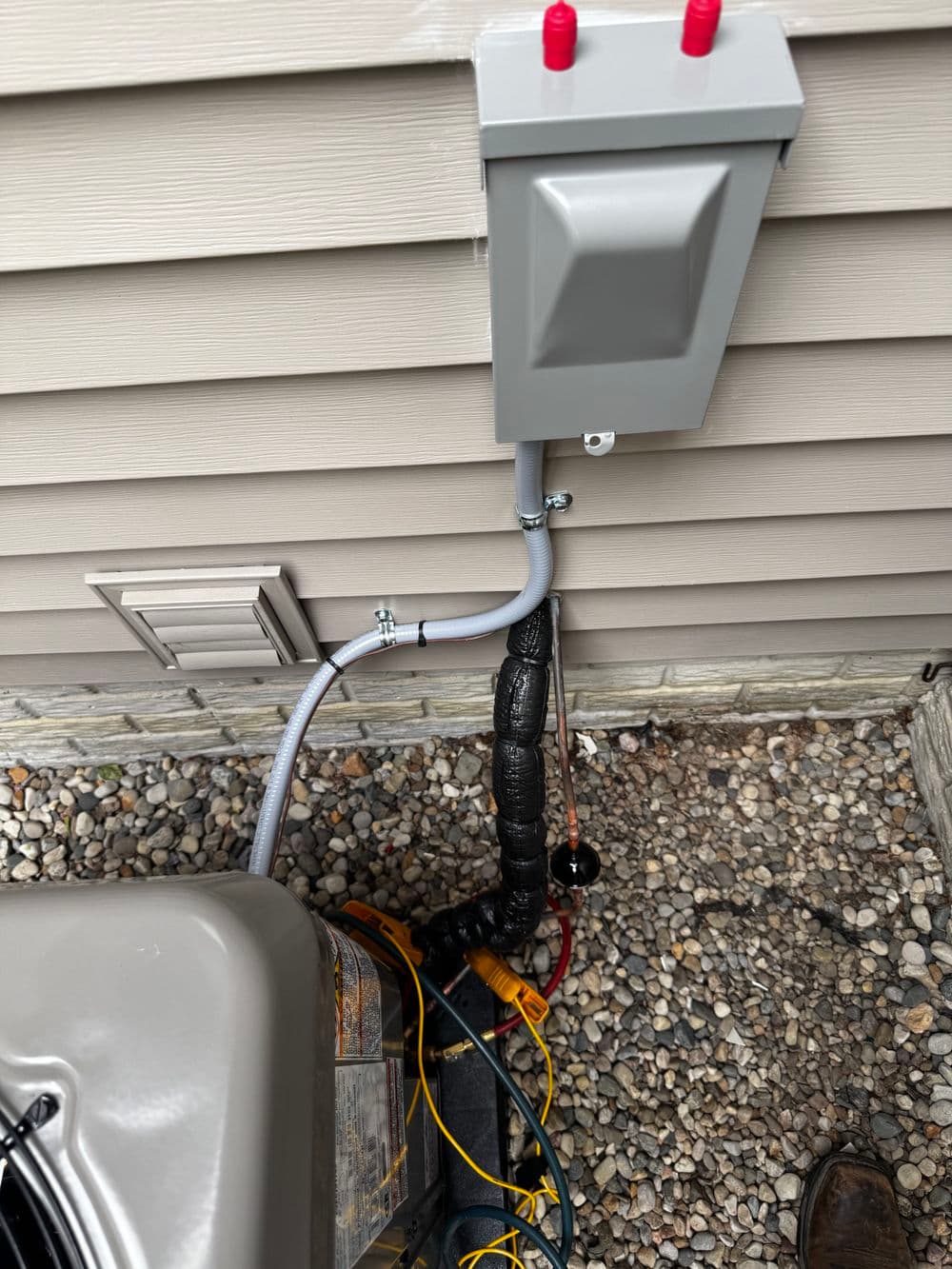 Electrical connection box beside an HVAC unit on a gravel surface, showing wiring details.