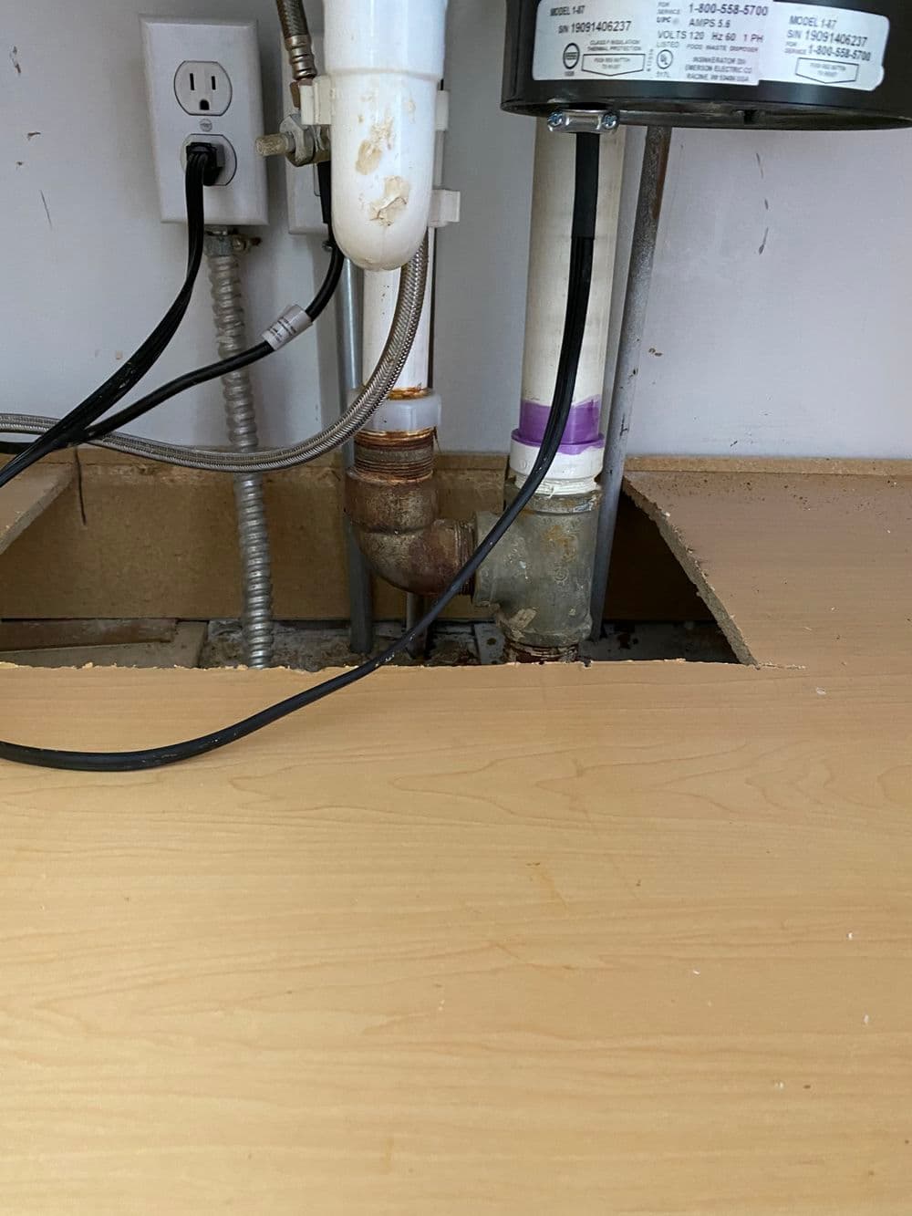 Under-sink plumbing setup with visible pipes and electrical outlet. Work surface partially removed.