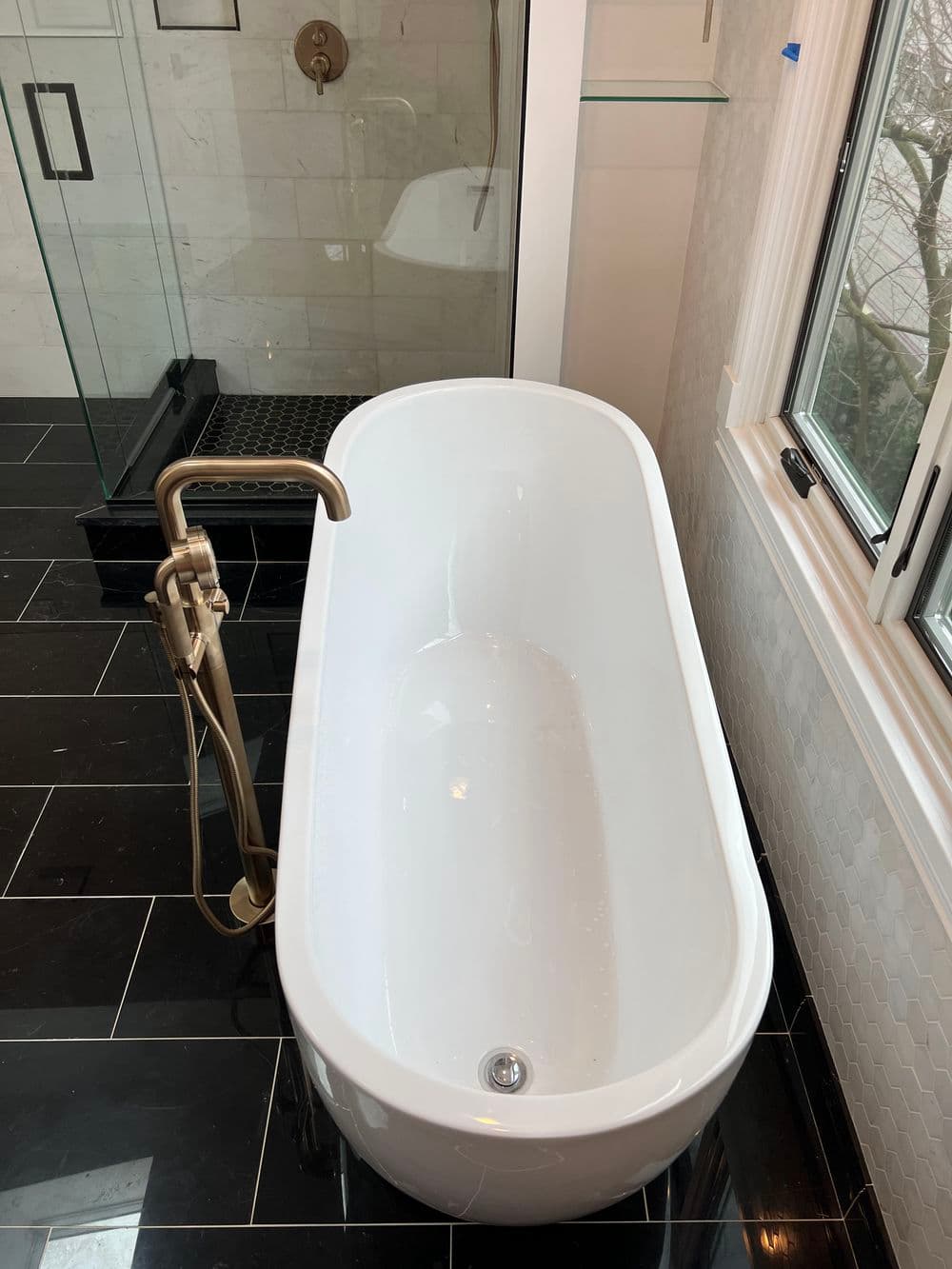 Modern freestanding bathtub in a luxury bathroom with dark tiles and glass shower.