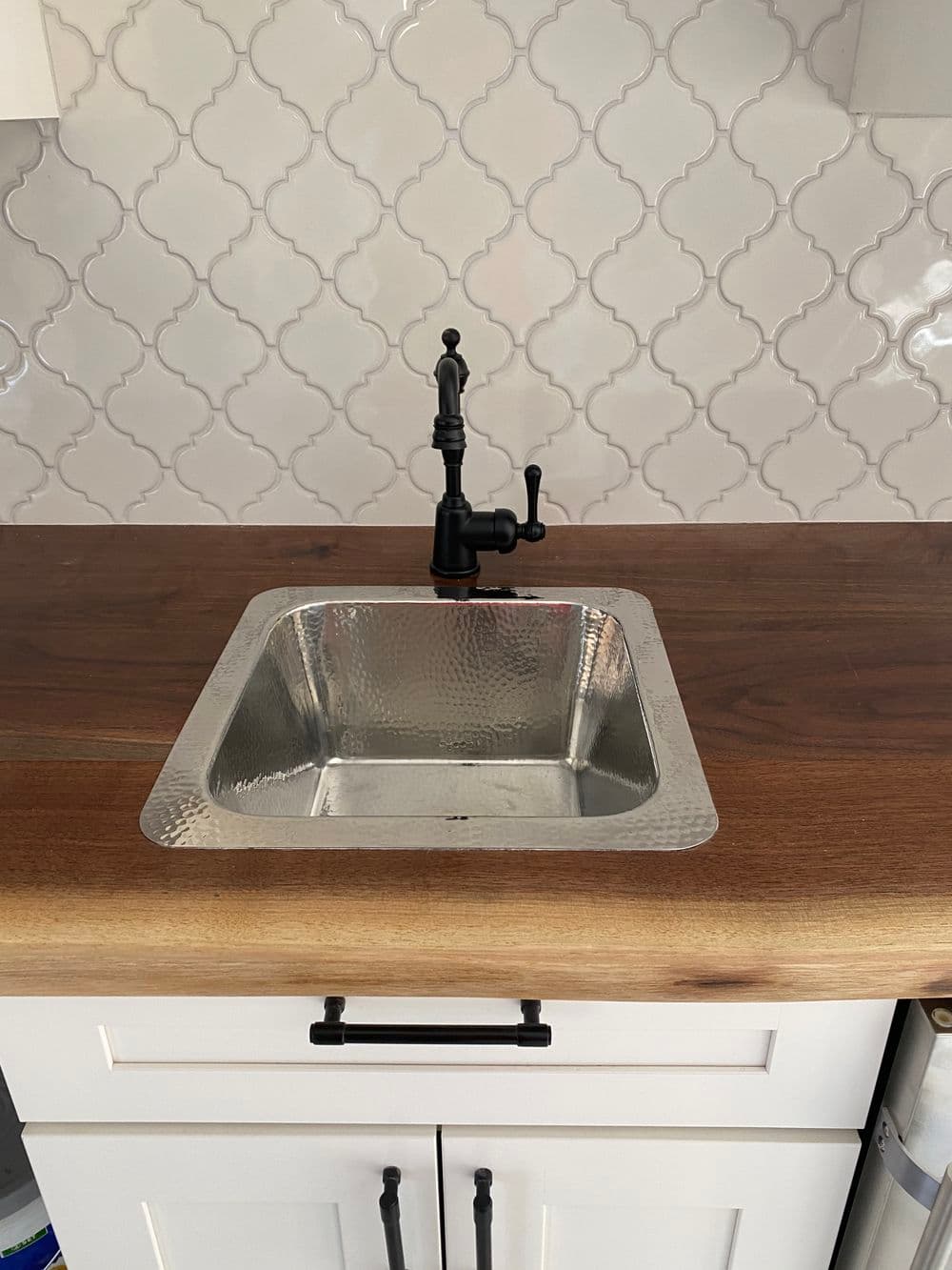 Modern kitchen with a square hammered metal sink and black faucet on wooden countertop.