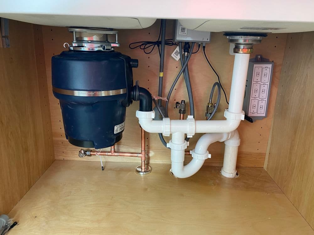Under-sink plumbing setup with garbage disposal, copper and PVC pipes, and electrical connections.