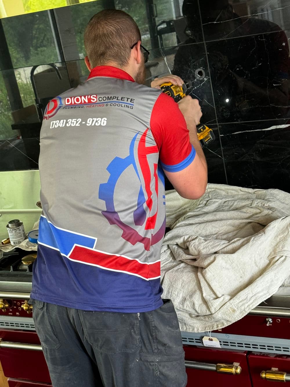 Technician in branded shirt using a drill on a home renovation project.