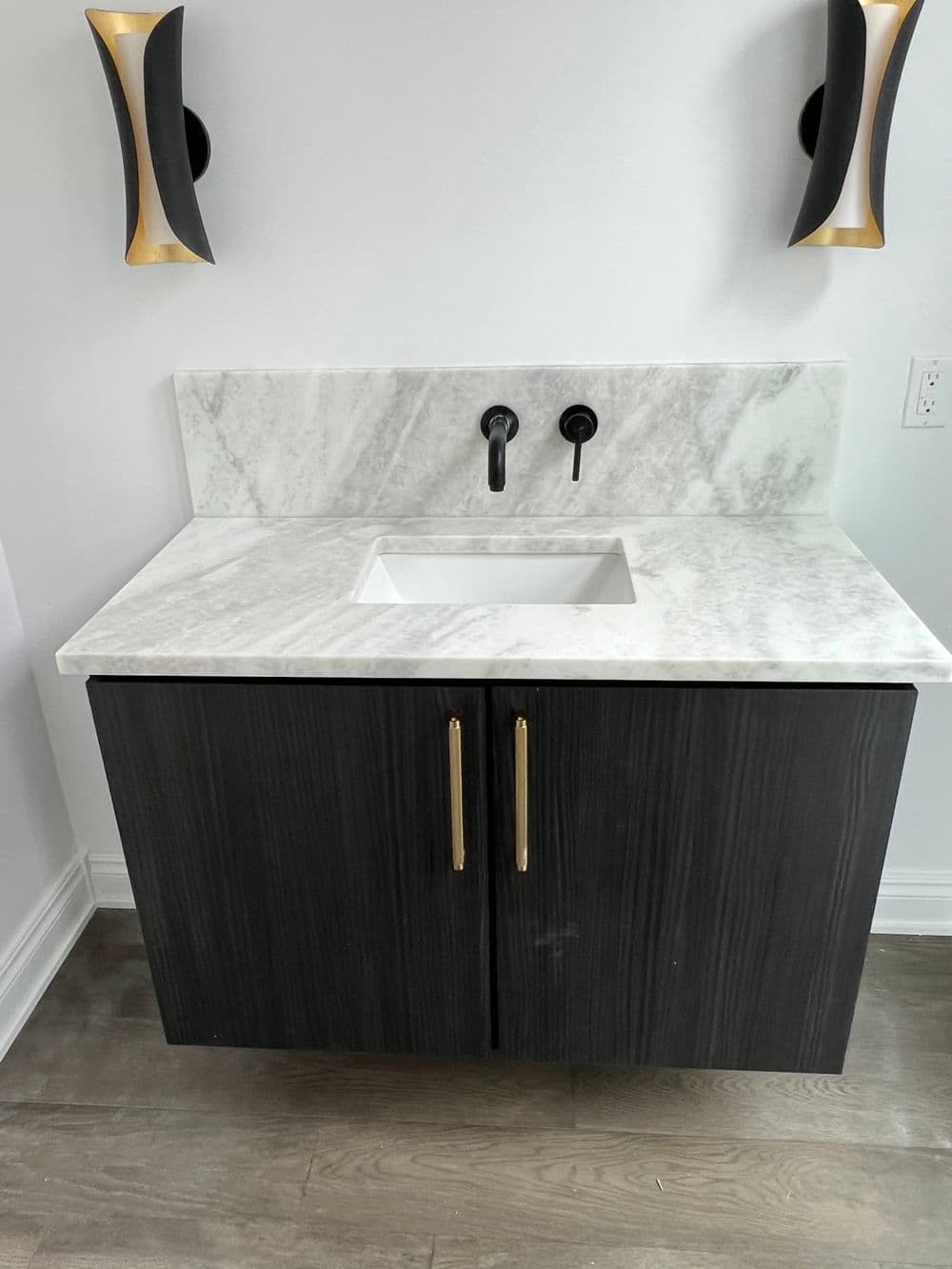 Modern bathroom vanity with a marble countertop and dark wood cabinet. Stylish wall sconces.