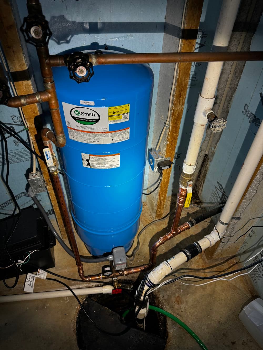Blue water heater tank in a basement with copper and PVC pipes.