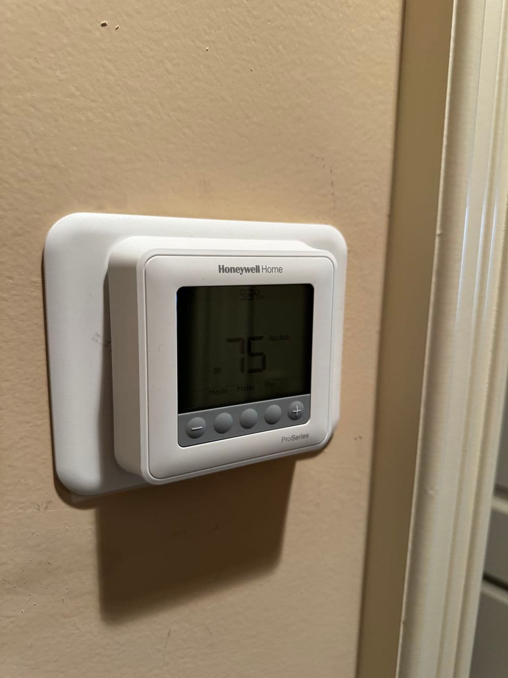 Honeywell Home programmable thermostat displaying 75 degrees on a beige wall.
