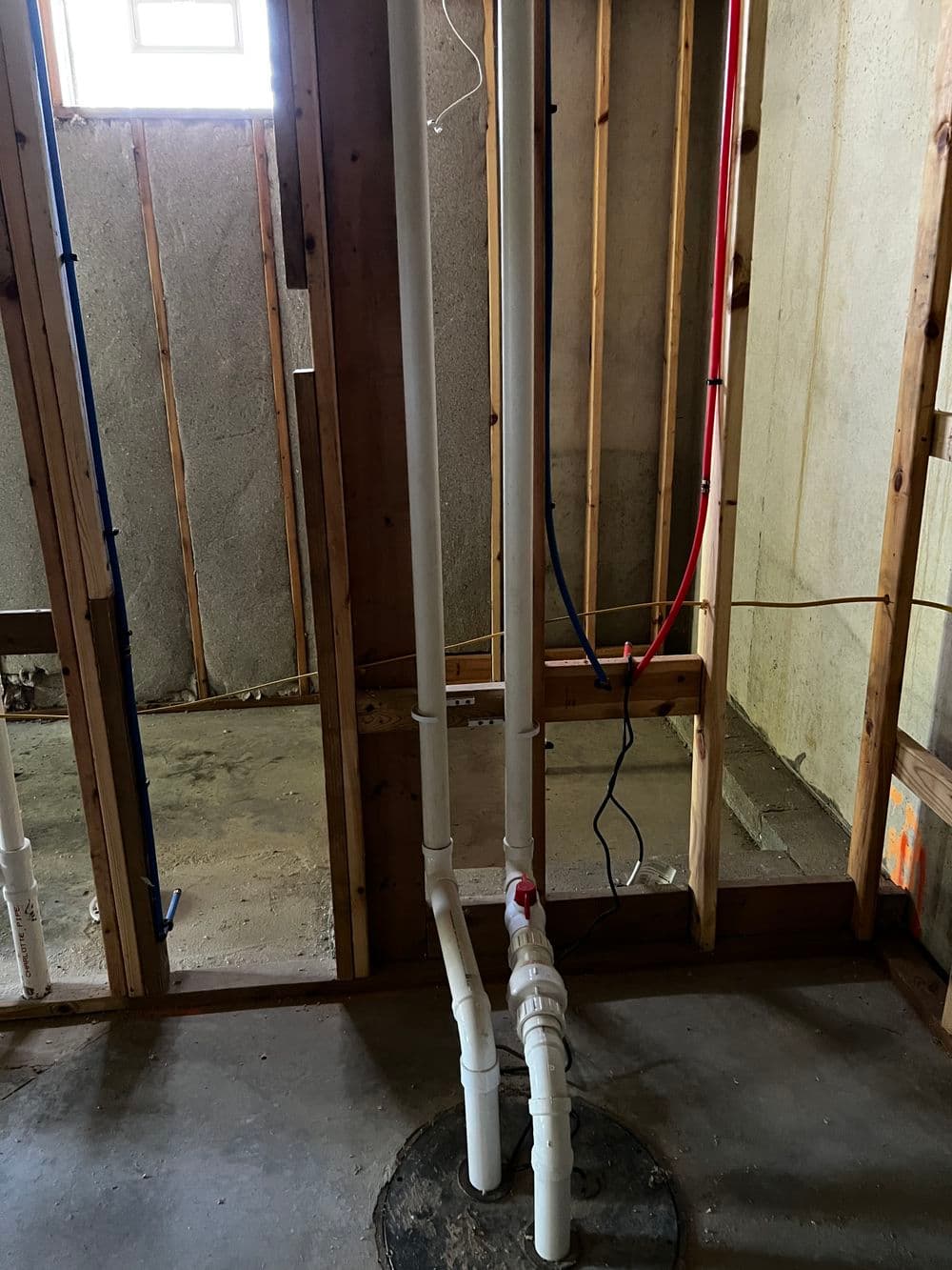 New basement plumbing installation with PVC pipes and electrical wiring visible.