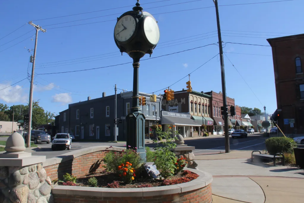 Street clock and flower planter on a downtown corner lined with brick storefronts